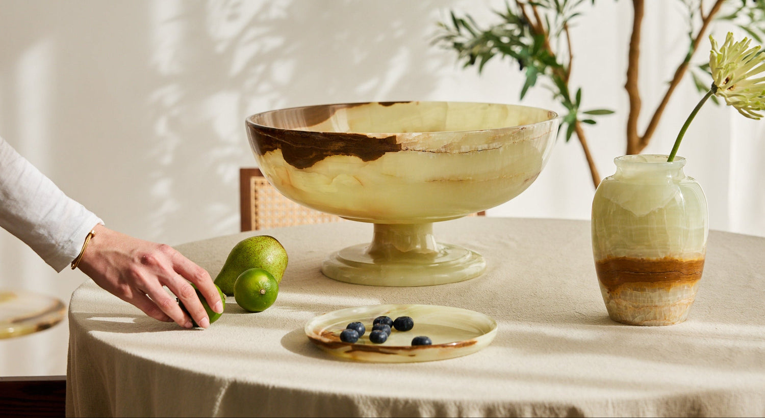 Table setting with a large decorative onyx bowl, small onyx vase, and fruit on a light surface
