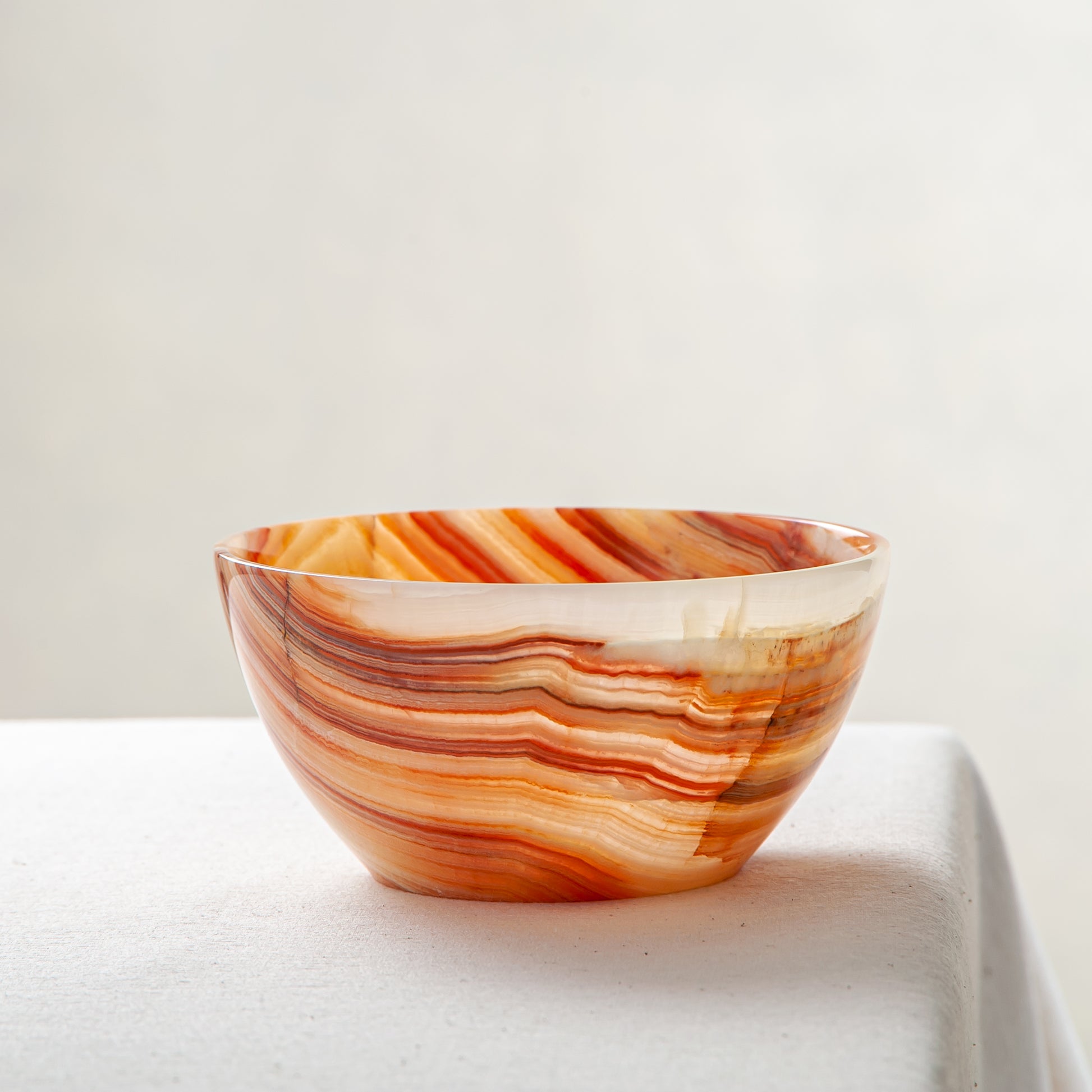 Unique natural onyx bowl in warm orange hues with translucent veining and smooth curved form
