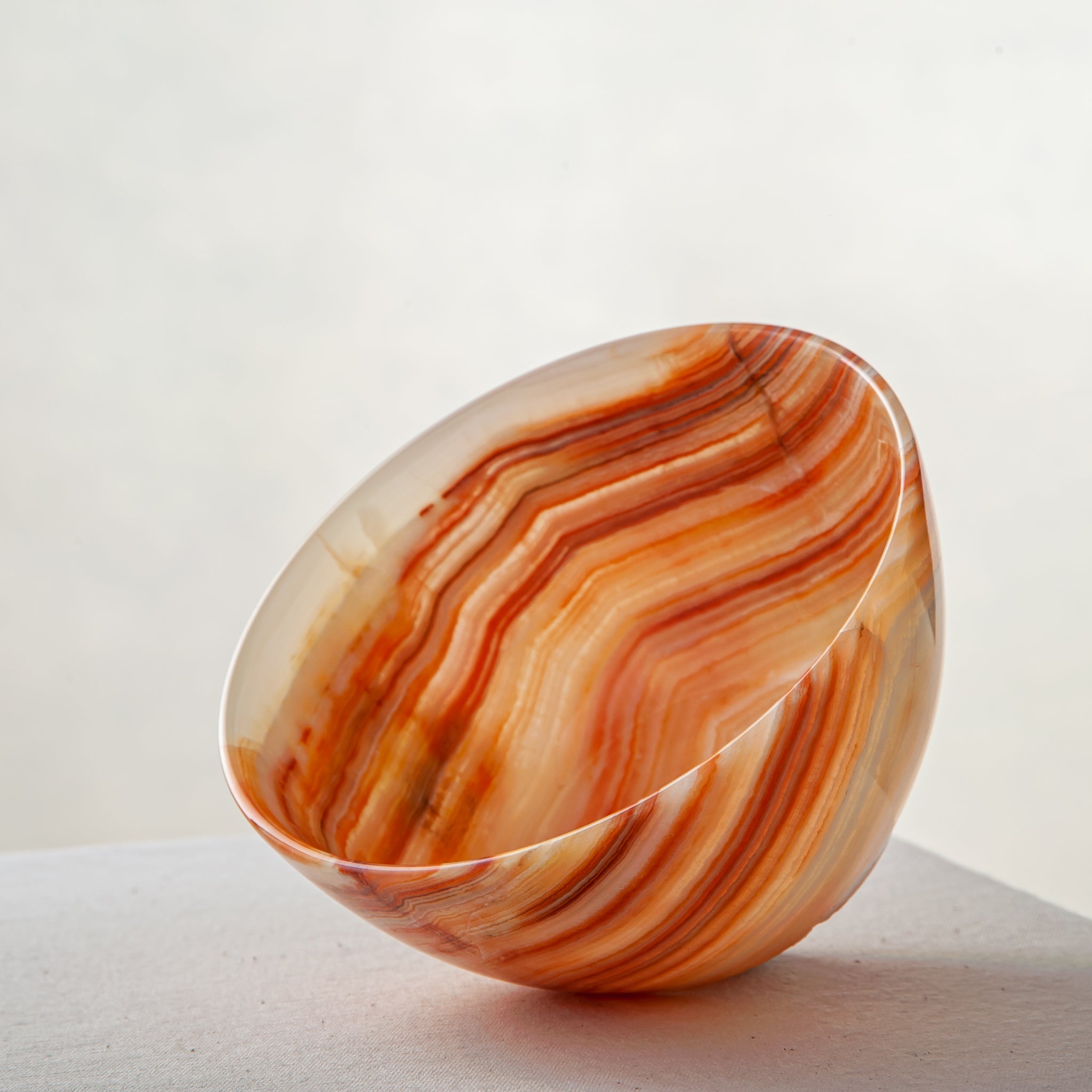 Unique natural onyx bowl in warm orange hues with translucent veining and smooth curved form

