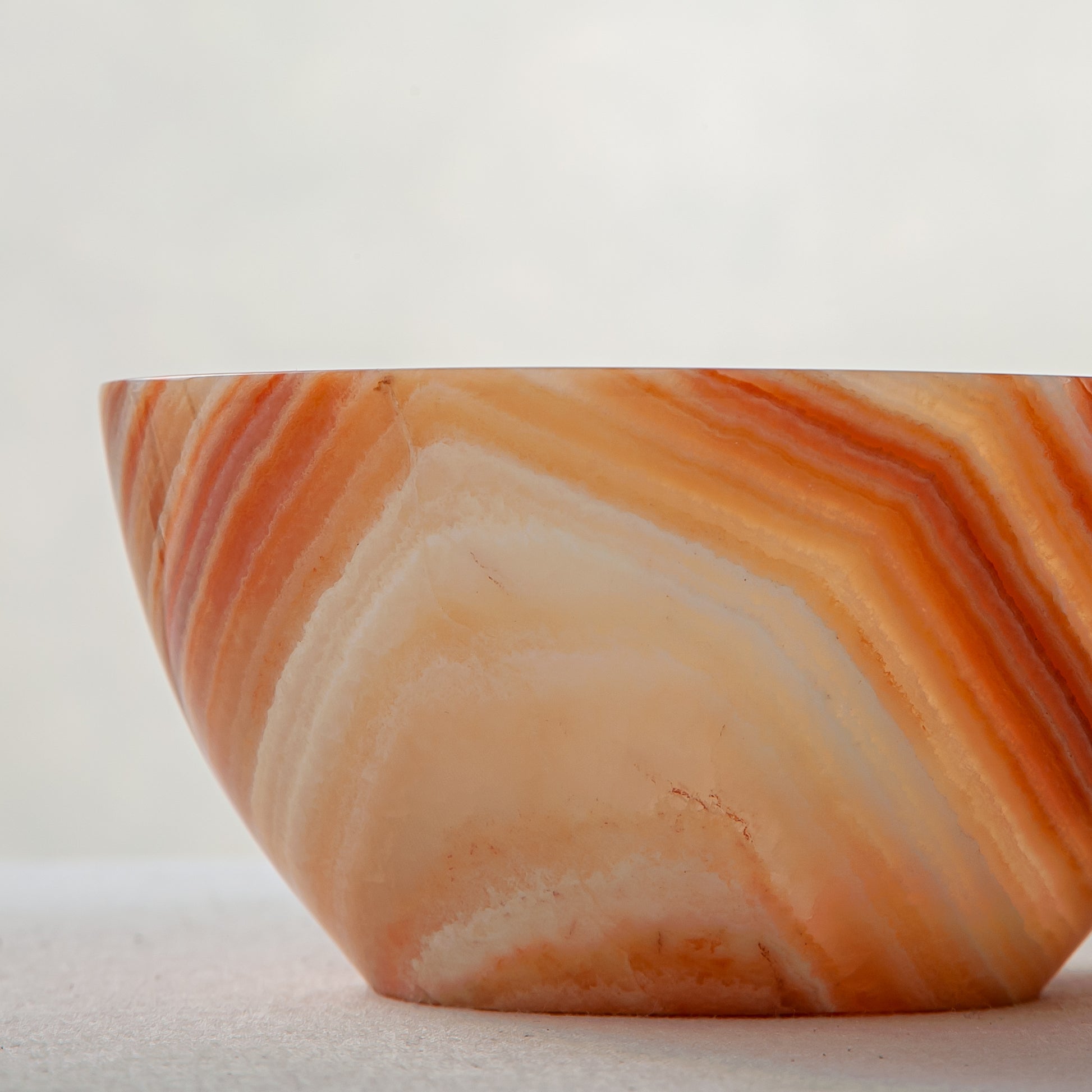 Unique natural onyx bowl in warm orange hues with translucent veining and smooth curved form
