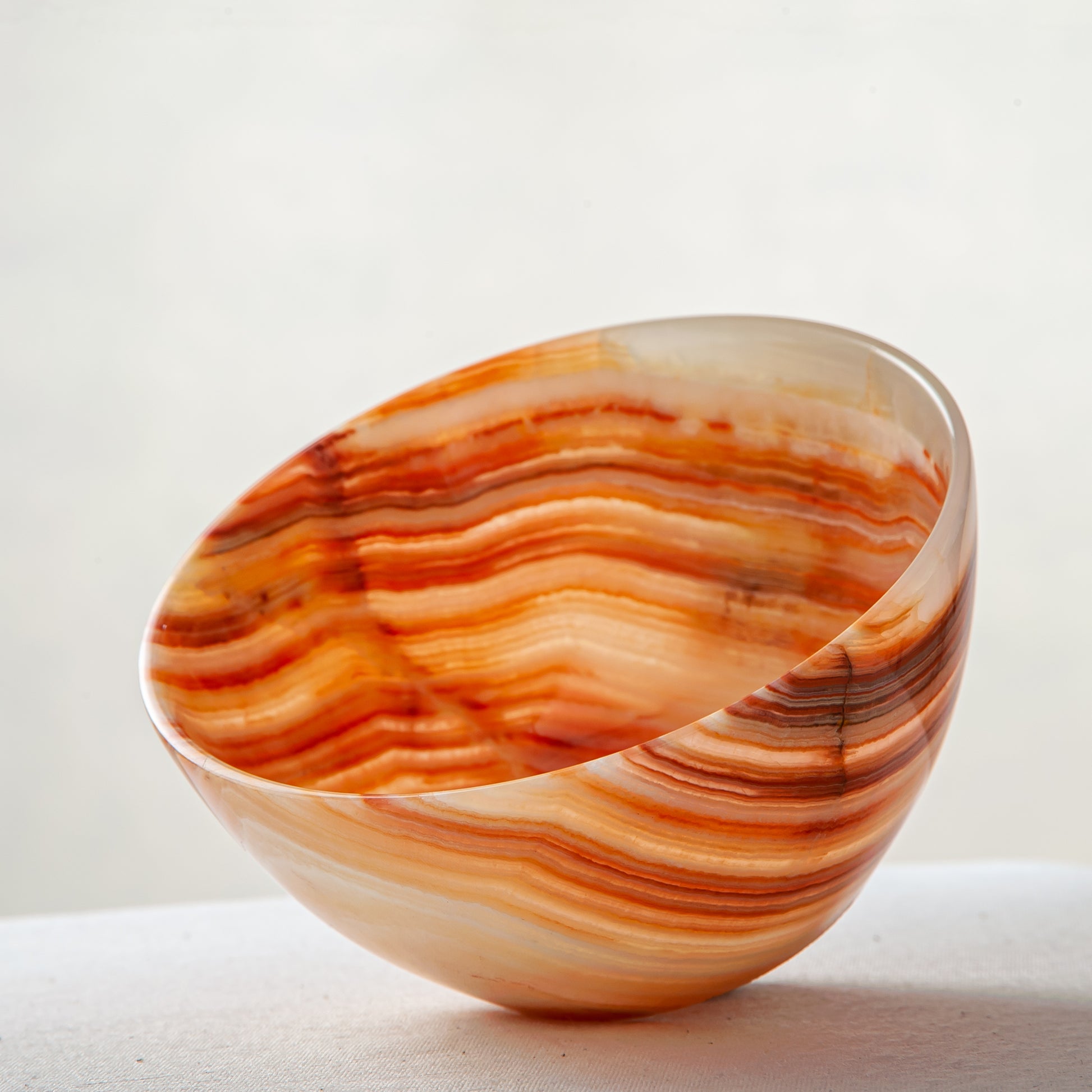 Unique natural onyx bowl in warm orange hues with translucent veining and smooth curved form
