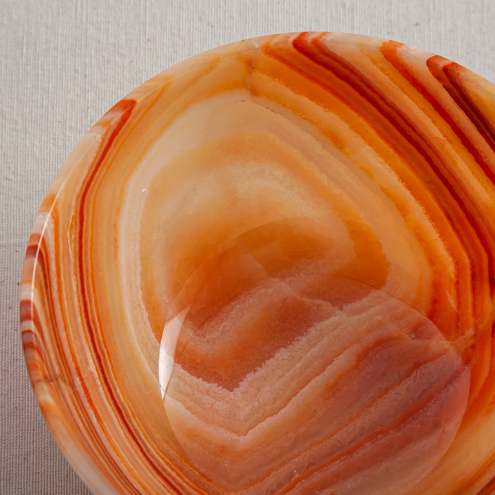 Unique natural onyx bowl in warm orange hues with translucent veining and smooth curved form
