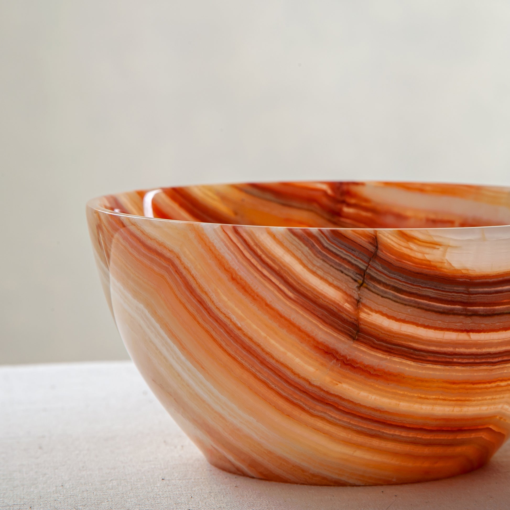 Unique natural onyx bowl in warm orange hues with translucent veining and smooth curved form

