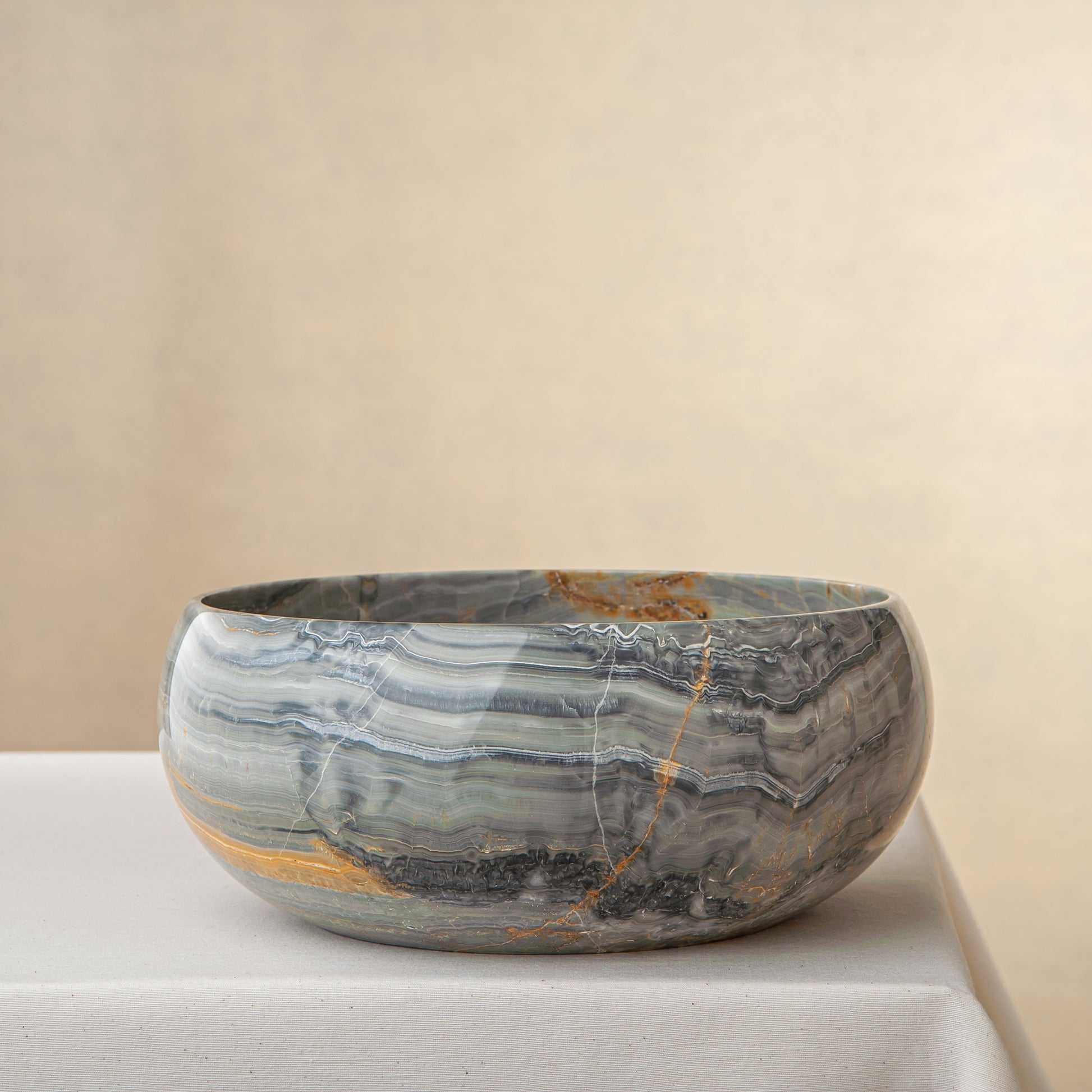 Handcrafted onyx bowl with grey blue banding and amber veining for luxury table decor
