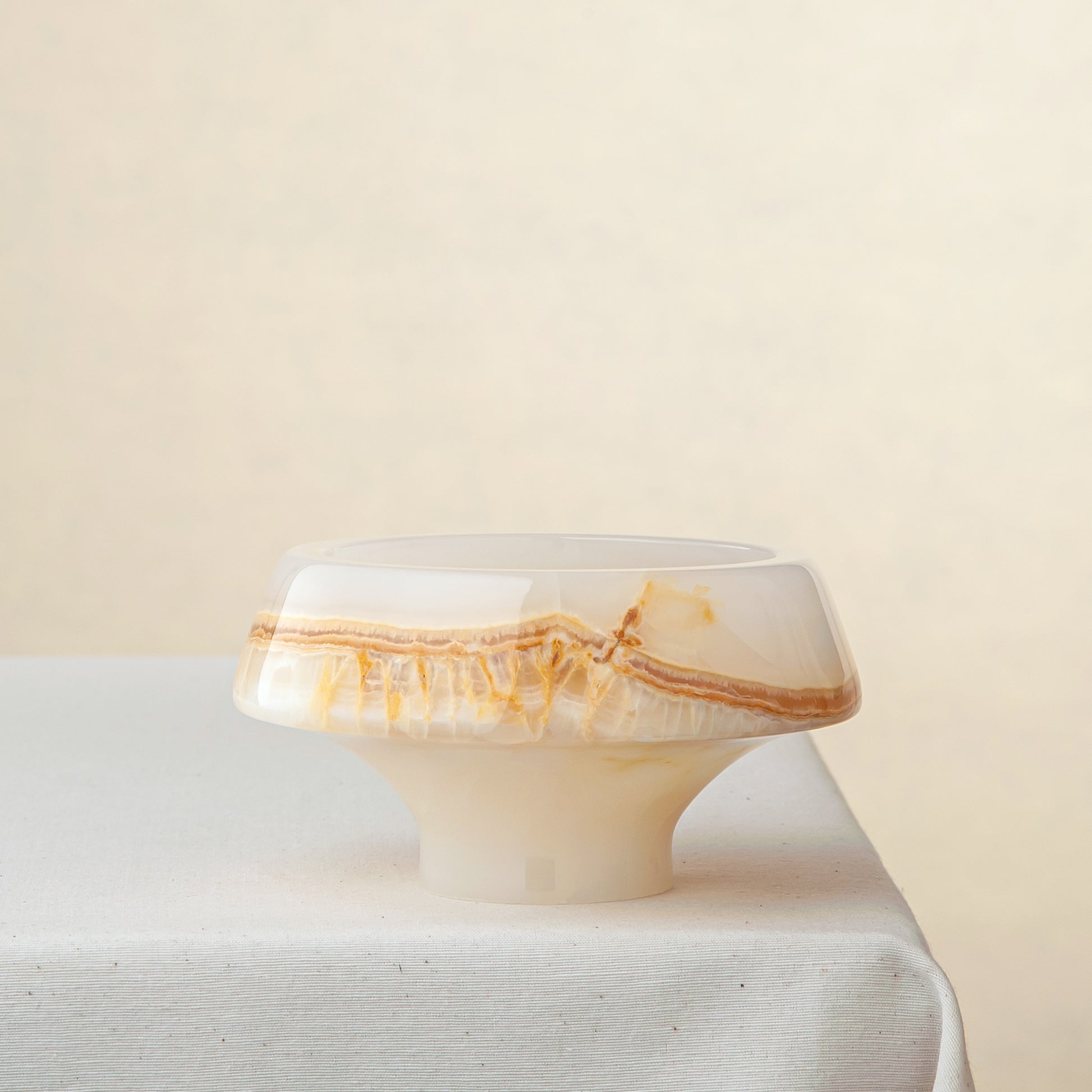 handcrafted onyx bowl with pedestal base and ivory surface with amber crystalline veining
