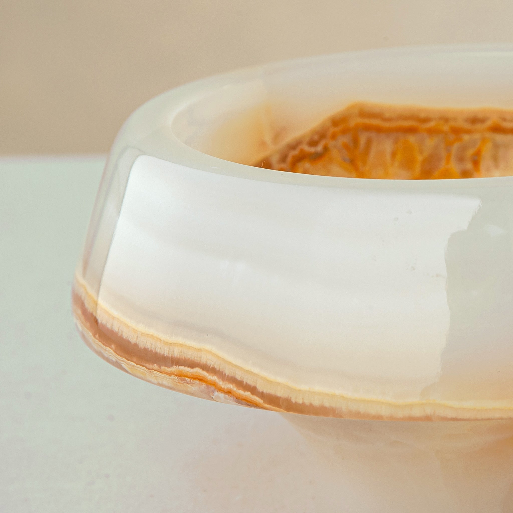 handcrafted onyx bowl with pedestal base and ivory surface with amber crystalline veining
