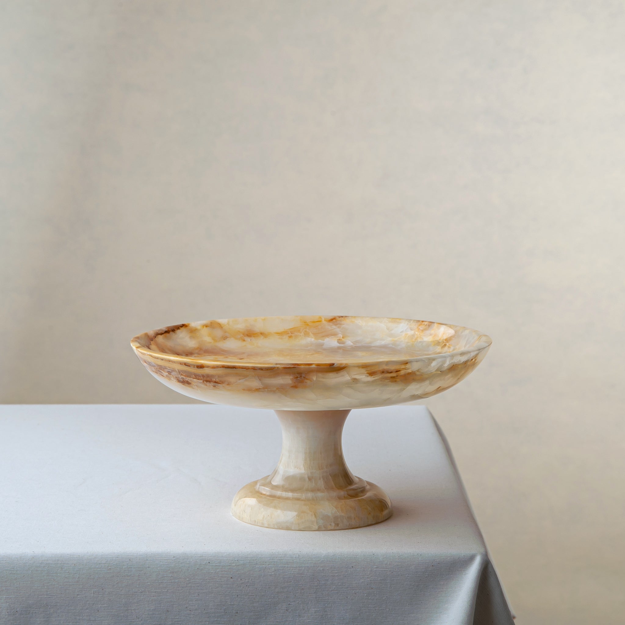 Handcrafted onyx cake stand with pedestal base in ivory and amber veining for elegant display
