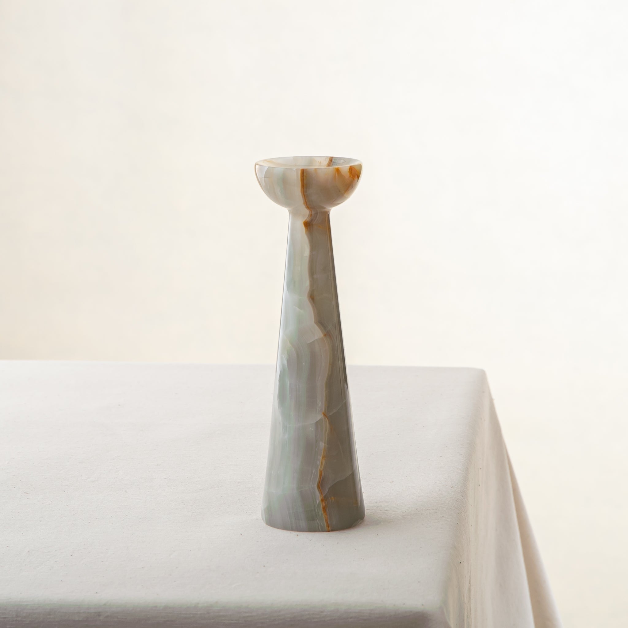 Handcrafted onyx candle holder with tall sculptural form and amber veining for modern decor
