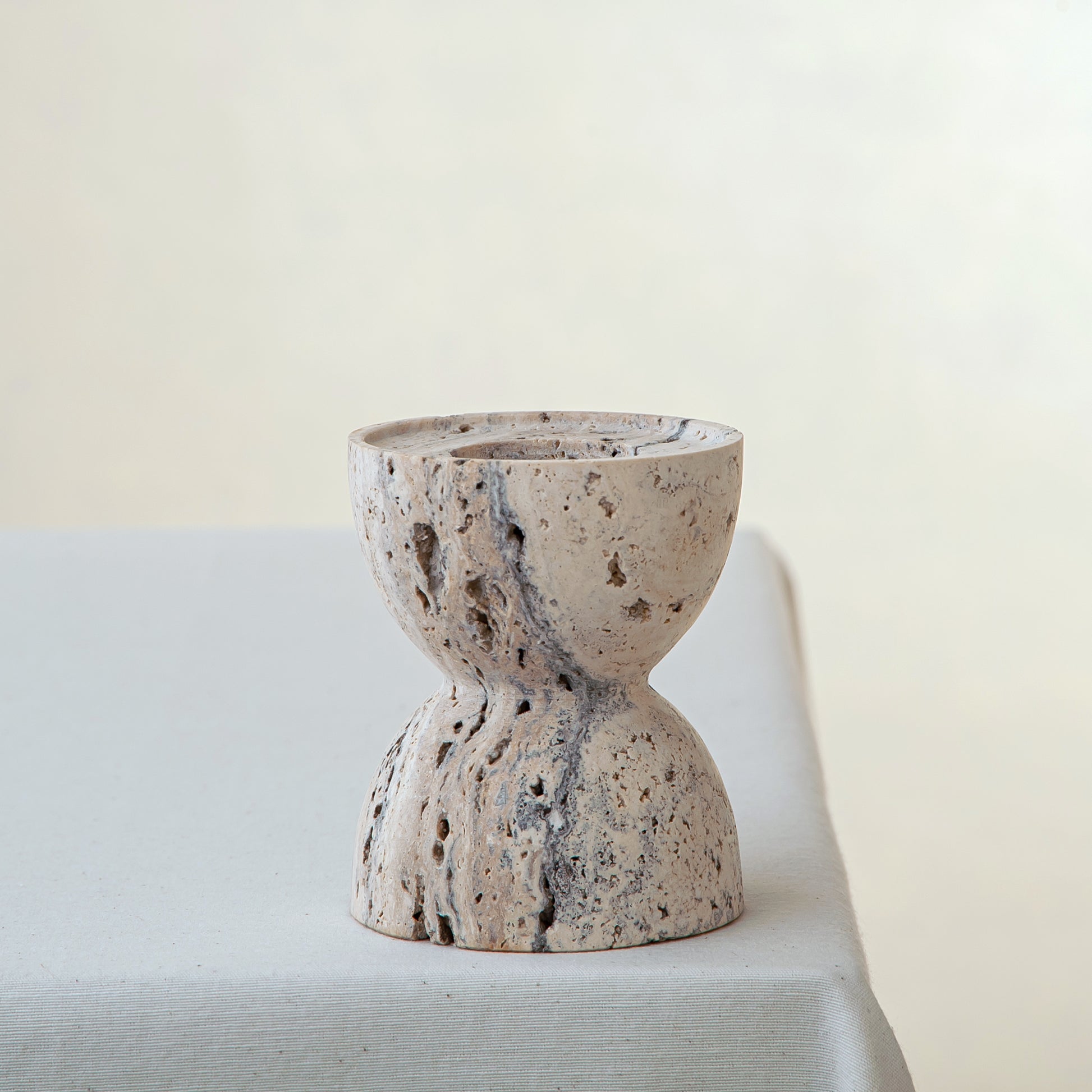 handcrafted travertine candle holder with porous texture and hourglass shape for modern decor
