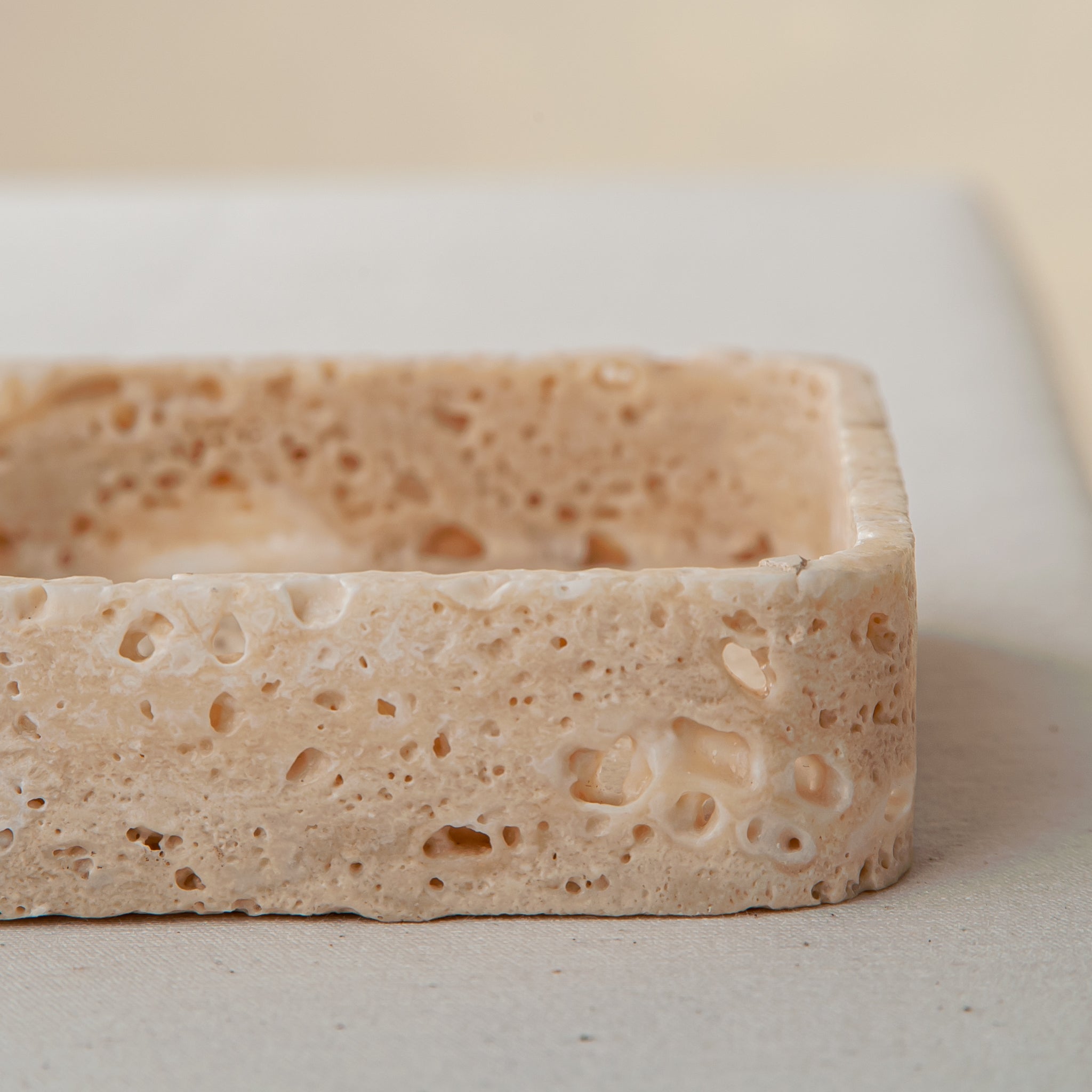 Handcrafted travertine tray with porous texture in soft beige tones as modern table decor
