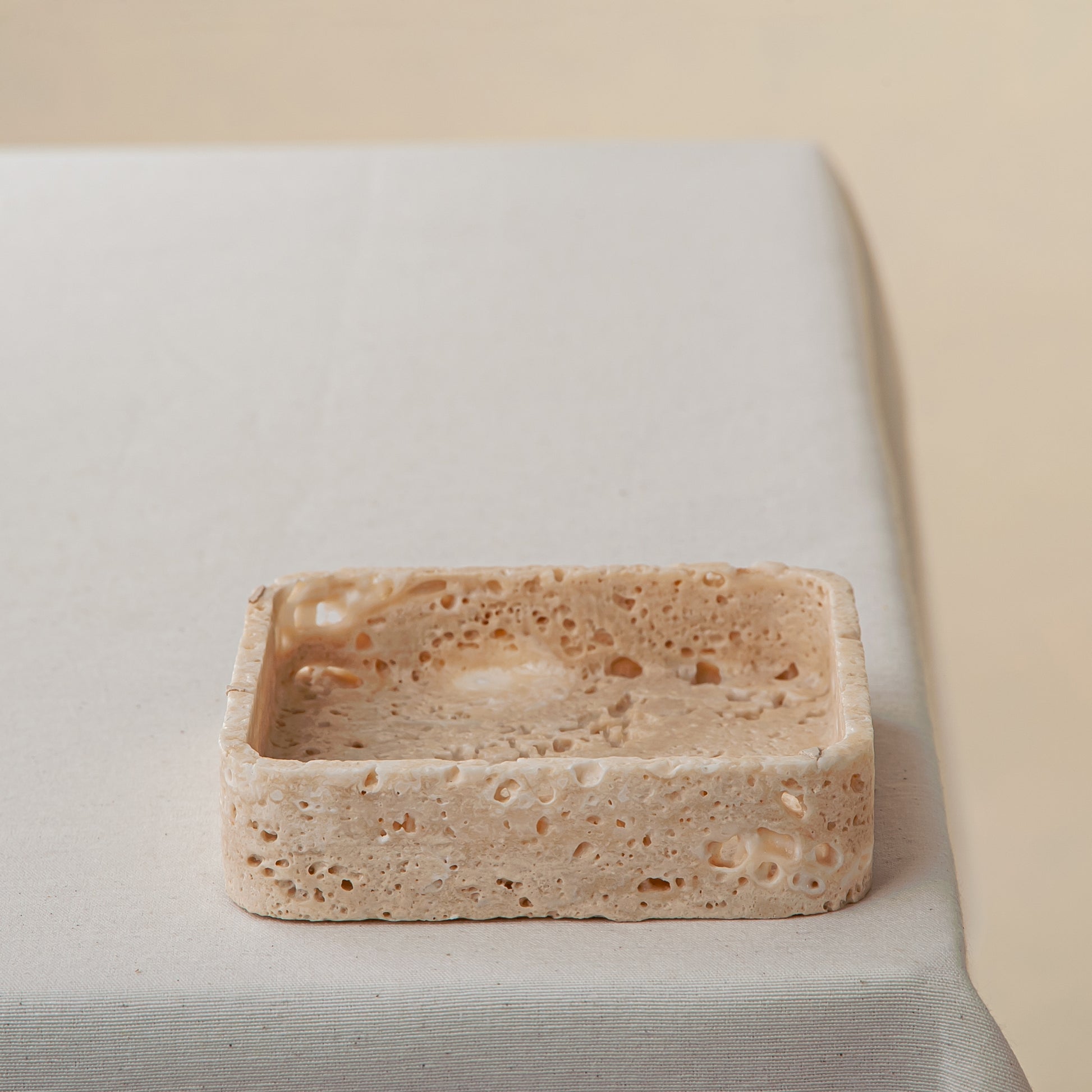 Handcrafted travertine tray with porous texture in soft beige tones as modern table decor
