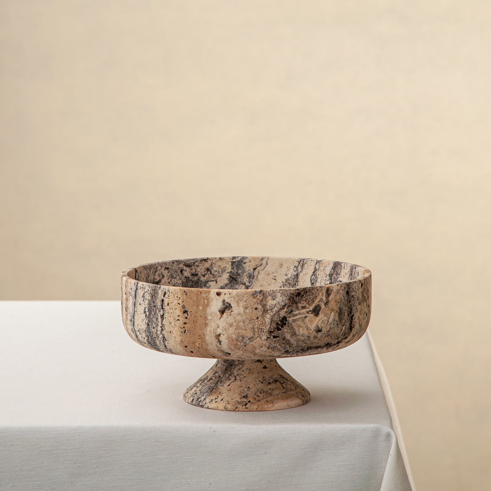 Handcrafted Gaia travertine bowl with wide shallow basin and pedestal base, featuring natural stone veining, by Uniiqo Studio